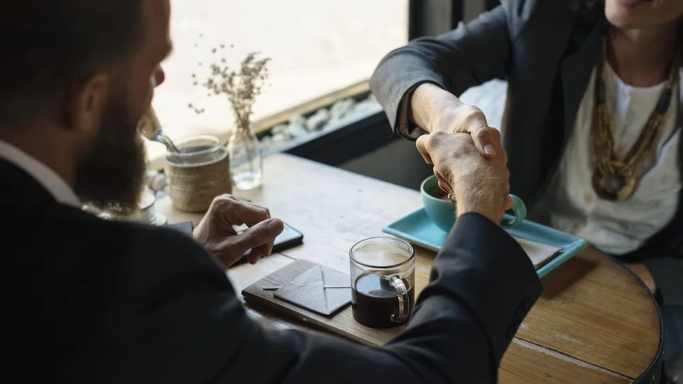 Two business people shaking hands on an agreement at a coffee shop